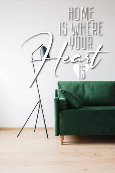Canapé vert avec oreiller près du lampadaire moderne et la maison est où votre cœur est lettrage — Photo de stock