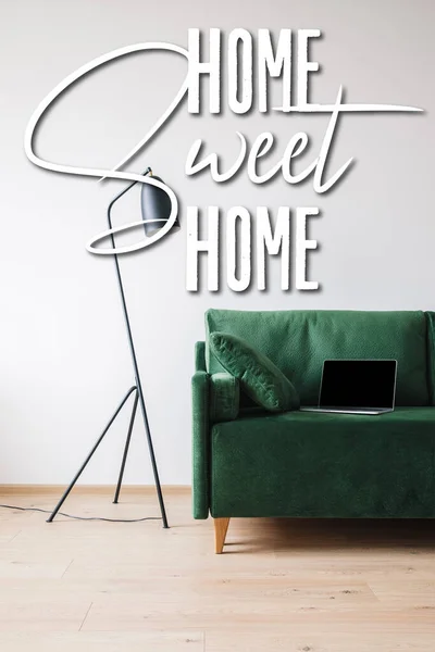 Laptop with blank screen on green sofa near floor lamp and home sweet home lettering — Stock Photo