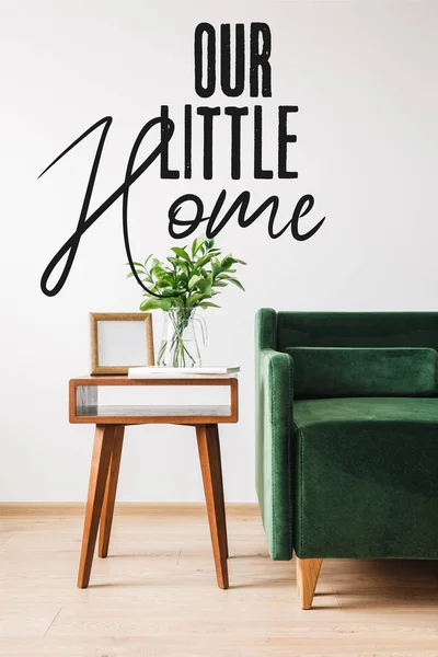 Green sofa near wooden coffee table with plant, books, photo frame and our little home lettering — Stock Photo