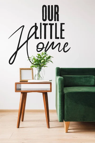 Sofá verde perto de mesa de café de madeira com planta, livros, moldura da foto e nossa pequena casa lettering — Fotografia de Stock