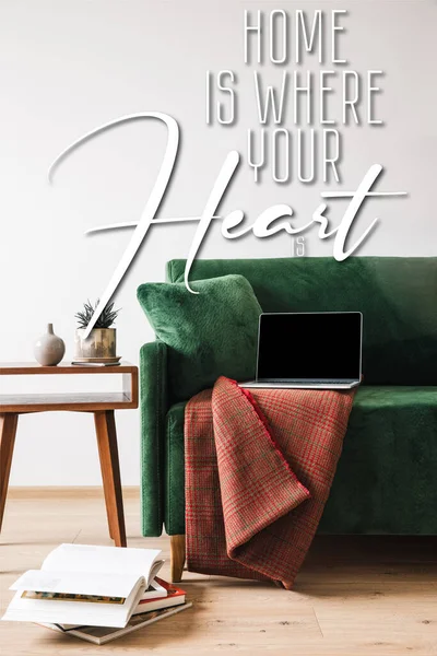 Green sofa with blanket and laptop near wooden coffee table and home is where your heart is lettering — Stock Photo