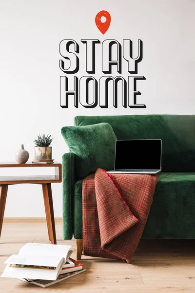 Grünes Sofa mit Decke und Laptop in der Nähe von Holztisch und zu Hause bleiben Schriftzug — Stockfoto