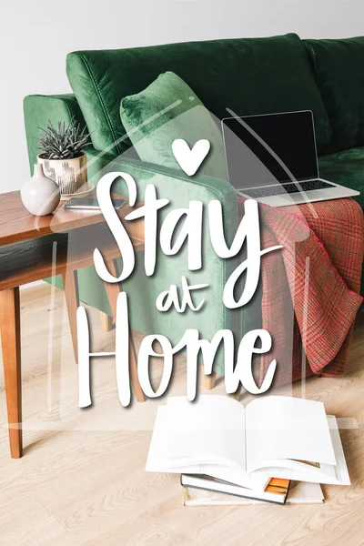 Canapé vert, couverture et ordinateur portable près de la table basse en bois avec plante et smartphone près de rester à la maison lettrage — Photo de stock