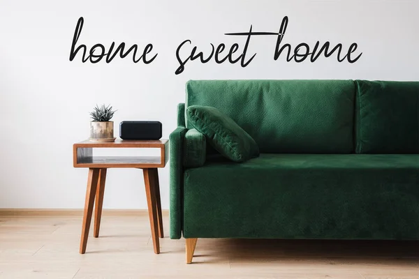 Canapé vert, oreiller, table basse en bois avec plante et réveil près de la maison lettrage doux maison — Photo de stock