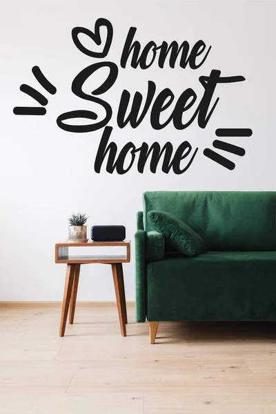 Divano verde moderno, cuscino, tavolino in legno con pianta e sveglia vicino casa dolce casa lettering — Foto stock