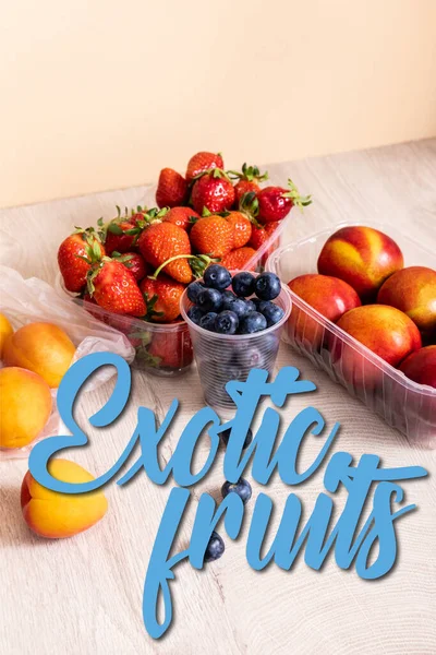 Blueberries, strawberries, nectarines and peaches in plastic containers near exotic fruits lettering on beige — Stock Photo
