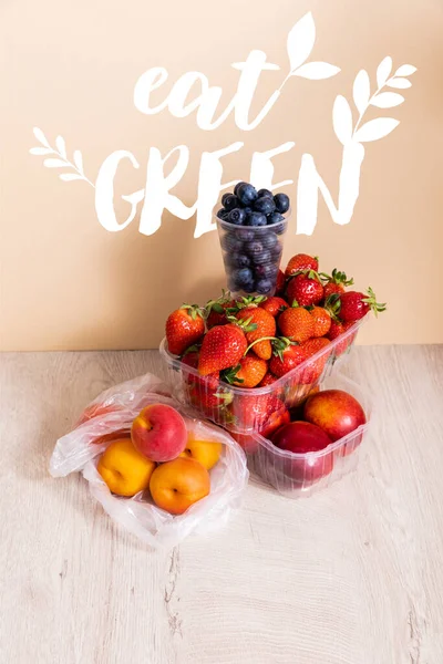 Composición de la fruta con arándanos, fresas, nectarinas y melocotones en envases de plástico cerca de comer letras verdes en beige - foto de stock