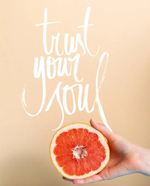 Abgeschnittene Ansicht der weiblichen Hand mit saftigen Grapefruit halb in der Nähe vertrauen Sie Ihrer Seele Schriftzug auf beige — Stockfoto