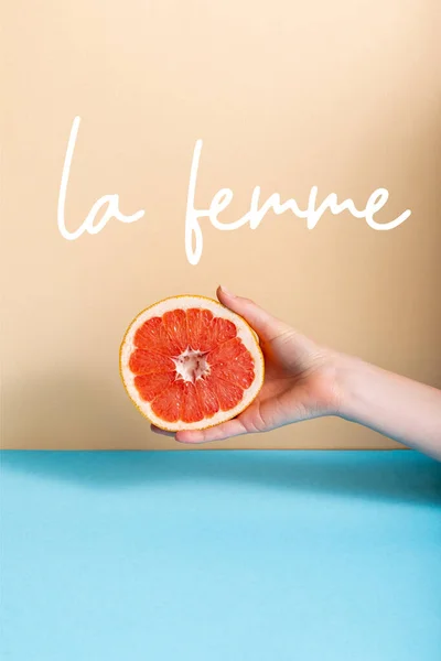 Vue recadrée de la main féminine avec moitié pamplemousse juteuse près de la femme lettrage sur beige et bleu — Photo de stock
