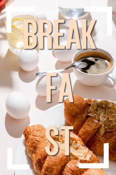 Boiled eggs, two croissants, cup of coffee and glass of water with lemon on grey table with breakfast lettering — Stock Photo