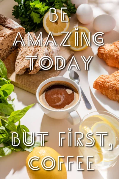 Fresh croissants, bread, greenery, eggs, lemon water and cup of coffee for breakfast on grey table with be amazing today, but first, coffee lettering — Stock Photo