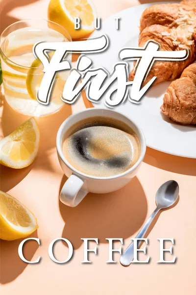 Кофейная чашка с чайной ложкой, круассаны и стакан воды с лимоном на завтрак на бежевом столе с но первый кофе буквы — стоковое фото