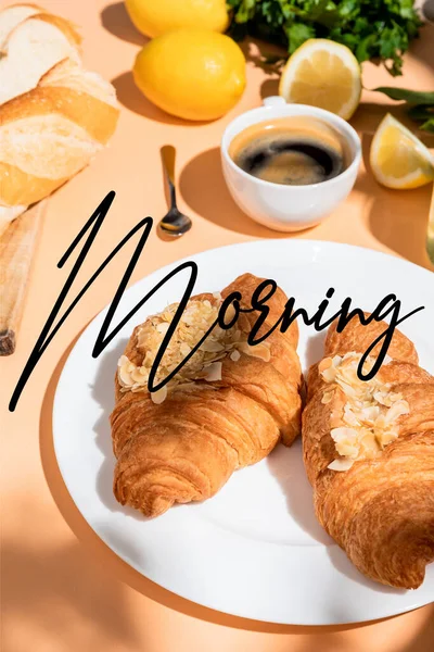 Croissants, baguete, limões e xícara de café no café da manhã em mesa bege com letras matinais — Fotografia de Stock