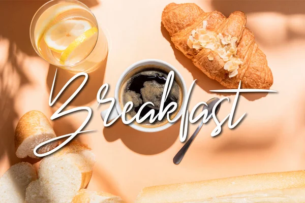 Vista superior de café, agua, baguette y croissant en la mesa beige con letras de desayuno - foto de stock