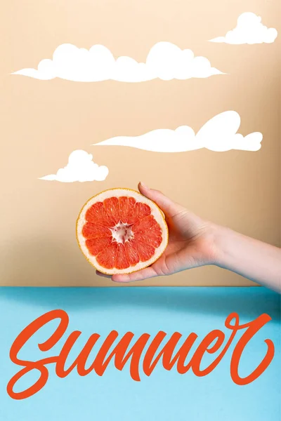 Cropped view of woman holding juicy half of grapefruit near summer lettering on beige and blue — Stock Photo