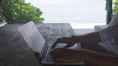 Çardak içinde oturan ve deniz manzaralı, statik kare, bilgisayarda çalışan mutlu adam yakın çekim