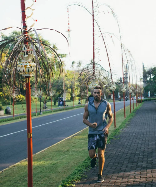 Strong and muscular man model running on the road, at sunset, in Asia