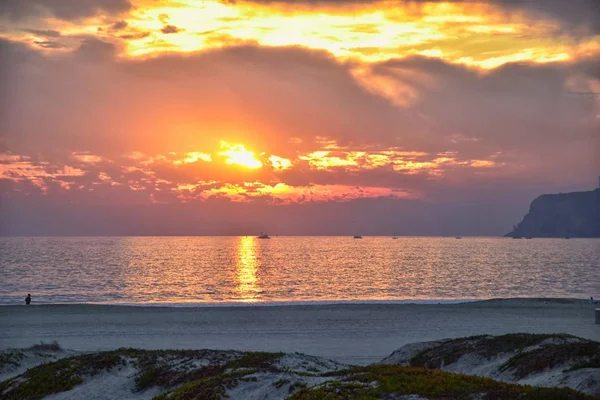 Coronado Beach in San Diego by the Historic Hotel del Coronado, at sunset with unique beach sand dunes, panorama view of the Pacific Ocean, silhouettes of people walking and boats in California, United States.