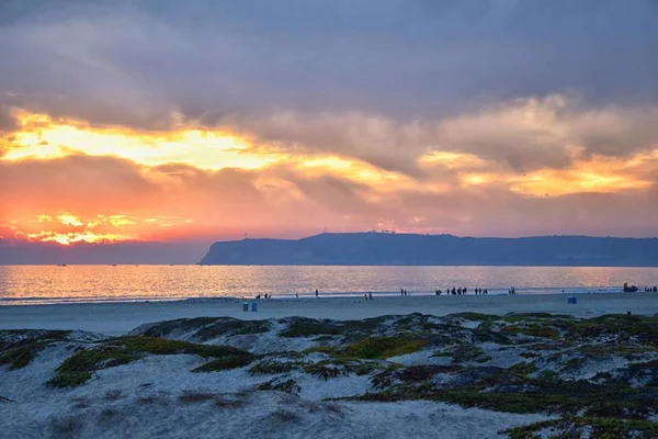 Coronado Beach in San Diego by the Historic Hotel del Coronado, at sunset with unique beach sand dunes, panorama view of the Pacific Ocean, silhouettes of people walking and boats in California, United States.