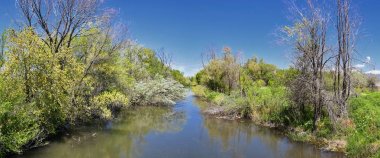 Jordan River Parkway Trail, Legacy Parkway Trail sınır Redwood Trailhead, kayalık dağlar boyunca çevredeki ağaçlar ve silt dolu çamurlu su ile panorama manzarası, Salt Lake City, Utah.