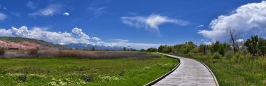 Jordan River Parkway Trail, Legacy Parkway Trail sınır Redwood Trailhead, kayalık dağlar boyunca çevredeki ağaçlar ve silt dolu çamurlu su ile panorama manzarası, Salt Lake City, Utah.