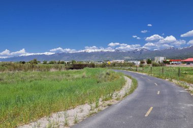 Jordan River Parkway Trail, Legacy Parkway Trail sınır Redwood Trailhead, kayalık dağlar boyunca çevredeki ağaçlar ve silt dolu çamurlu su ile panorama manzarası, Salt Lake City, Utah.
