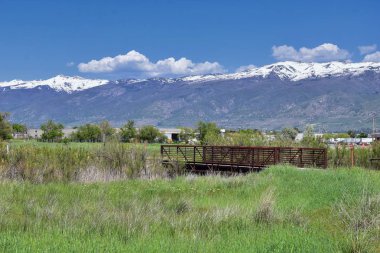 Jordan River Parkway Trail, Legacy Parkway Trail sınır Redwood Trailhead, kayalık dağlar boyunca çevredeki ağaçlar ve silt dolu çamurlu su ile panorama manzarası, Salt Lake City, Utah.