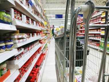 Ürünlerle dolu raflar arasında bir alışveriş arabası 