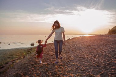 Anne ve kızı sahilde günbatımı sırasında yürüyüş. Mutlu bir dostu aile kavramı.