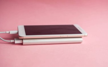 Beyaz akıllı telefon şarj cihazı ile şarj cihazı gücü banka pembe bir arka plan üzerinde