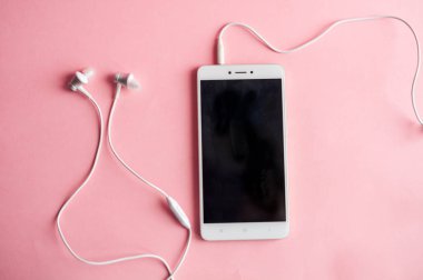 Kulaklıklar üzerinde pembe bir arka plan ile bir akıllı telefon yakın çekim. Yukarıdan görüntüleyin. Müzik dinlemek