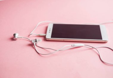 Kulaklıklar üzerinde pembe bir arka plan ile bir akıllı telefon yakın çekim. Yukarıdan görüntüleyin. Müzik dinlemek