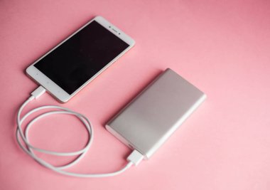 Beyaz akıllı telefon şarj cihazı ile şarj cihazı gücü banka pembe bir arka plan üzerinde