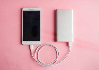 Beyaz akıllı telefon şarj cihazı ile şarj cihazı gücü banka pembe bir arka plan üzerinde