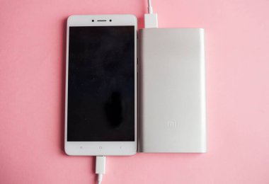 Beyaz akıllı telefon şarj cihazı ile şarj cihazı gücü banka pembe bir arka plan üzerinde