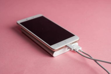 Beyaz akıllı telefon şarj cihazı ile şarj cihazı gücü banka pembe bir arka plan üzerinde