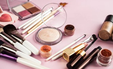 Pembe arka planda makyaj fırçası ve kozmetik ürünleri..