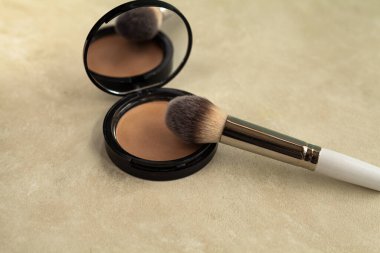 Kozmetik - makyaj tozu ve kırık bir fondöten ile birlikte bej arka planda bir fırça.