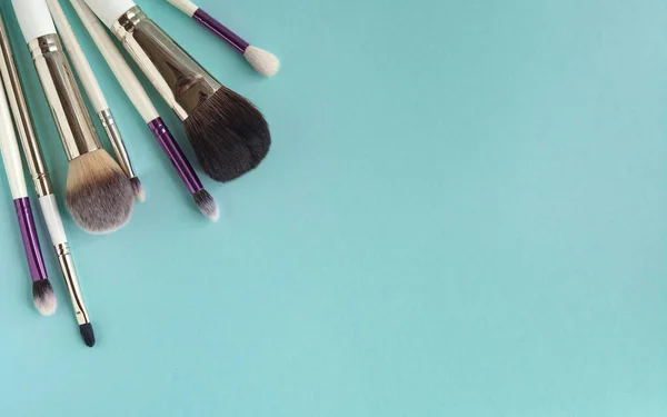 Makeup brushes, everyday makeup products. Cosmetic items on blue background, close up, copy space.