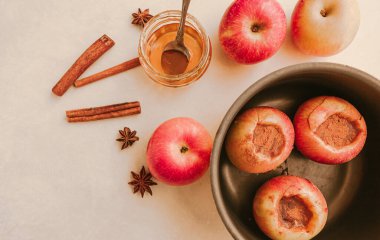 Bal ve tarçınla doldurulmuş fırınlanmış elmaları bej bir arka planda, yuvarlak bir kabın içinde pişirmek. Yukarıdan görüntüle.