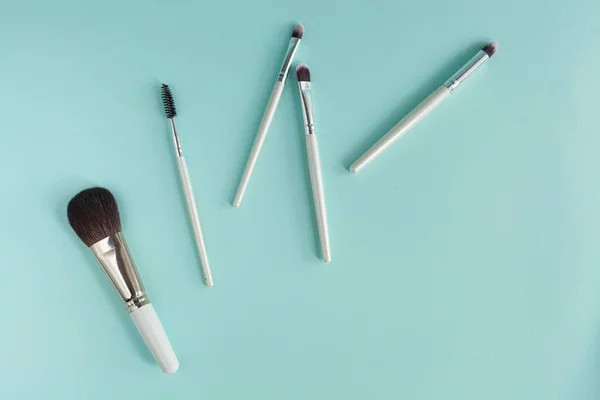 Makeup brushes, everyday makeup products. Cosmetic items on a blue background, close up