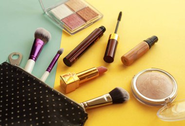 Parlak sarı ve mavi arka planda siyah kozmetik çantadan düşen makyaj ürünleri