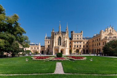 Lednice, Çek Cumhuriyeti - 14 Ağustos 2025: Bahçe bahçesi ve çiçek tarhı olan tarihi Lednice Şatosu binası, mavi gökyüzü ve mimariye hayran turistler.