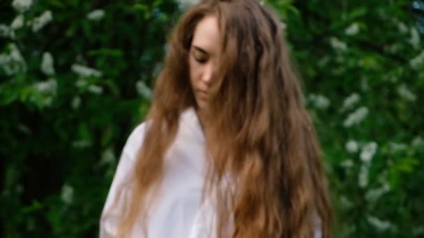 Hermosa joven con el pelo largo rizado oliendo una flor en la naturaleza. Movimiento de la cámara sobre una mujer en cámara lenta — Vídeos de Stock