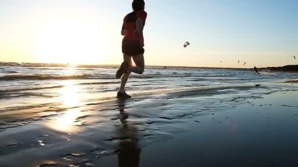 Homem corre na água no mar contra o pano de fundo de kitesurfers ao pôr do sol, câmera lenta — Vídeo de Stock