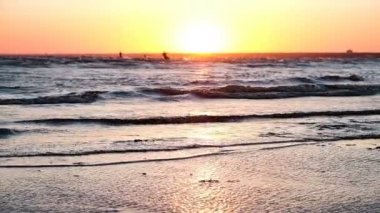 Arka planı kitesurfers, ağır çekim gün batımında kumsal dalgalar deniz yıkama.