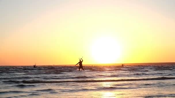 Kitesurfer prepares to skate, goes with a parachute in the water and raises the board at sunset in the summer, slow motion — Stock Video