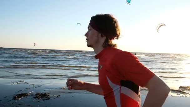 Man kör på stranden på en bakgrund av kitesurfare vid solnedgången eller morgon, slowmotion. Närbild — Stockvideo