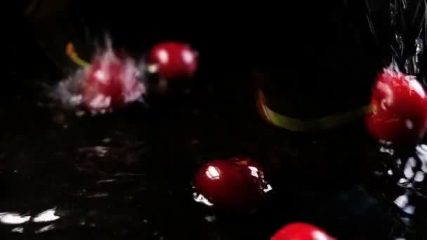 Cherries fall on the water on a black background and bounce off the surface, slow motion — Stock Video