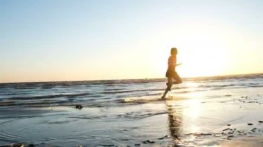 Sahilde denize koşan adam ve ellerini yukarı bitiş günbatımında yükseltir